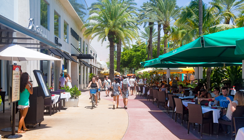Photo of a sidewalk in a retail and restaurant area with people walking and cycling