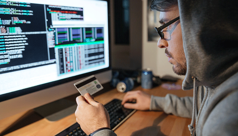 man seated at computer with terminal windows open copying information on back of credit card