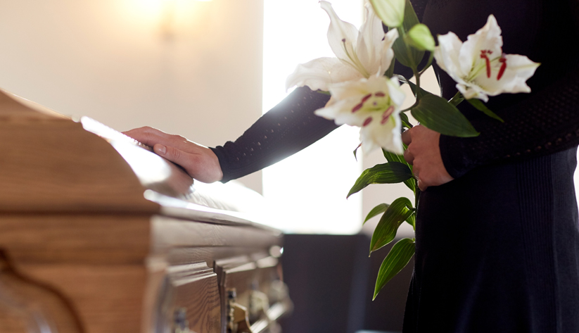 person at funeral with flowers putting hand on casket