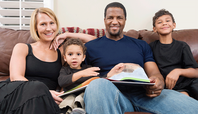 family of 4 sitting on couch with book open