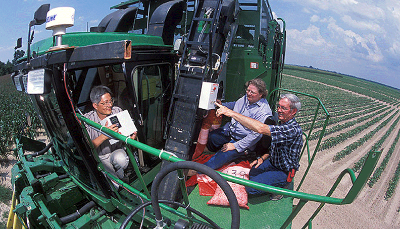 three farmers sitting atop a large harvester