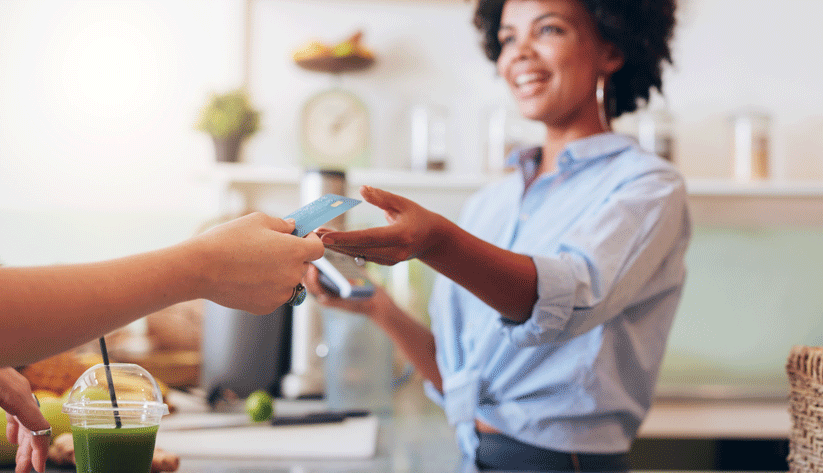 photograph of a customer handing a payment card to a smiling merchant at a cafe or juice bar