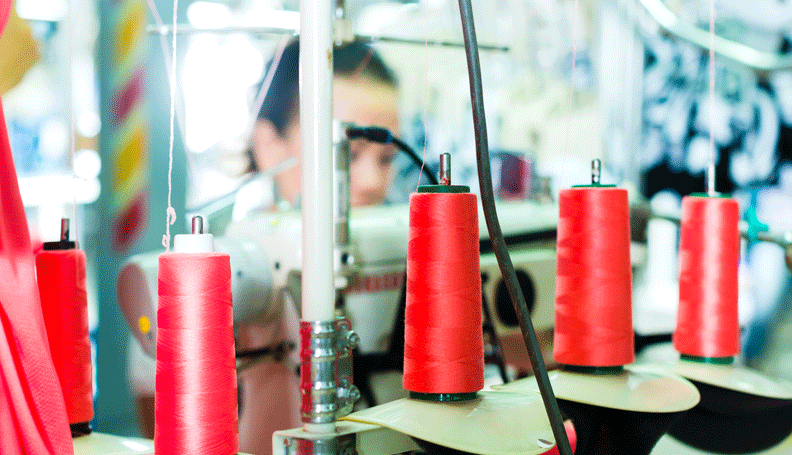 a clothing factory with red spools of thread in the foreground and a female worker in the background