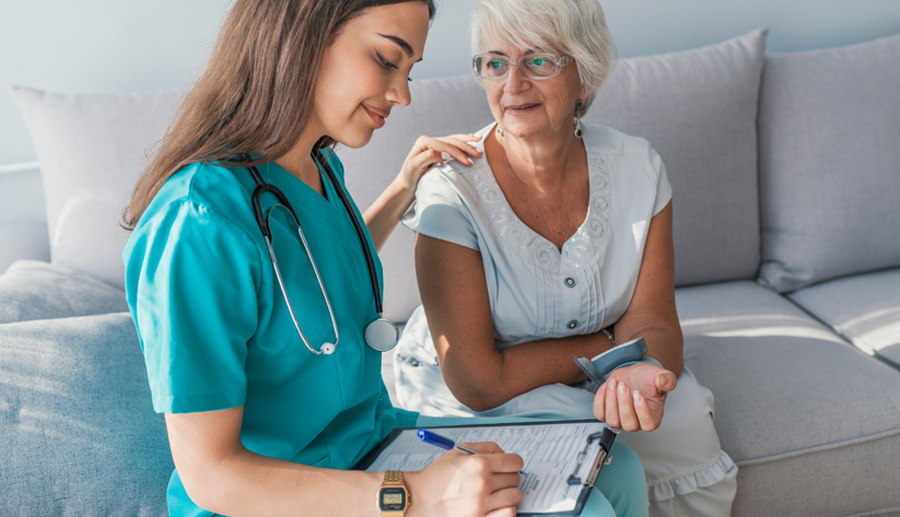 photograph of a younger female nurse sitting with an older female patient as her vitals are read