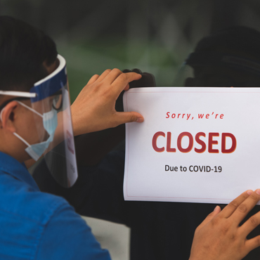 Photo of a man wearing a face shield hanging up a sign saying sorry we're closed