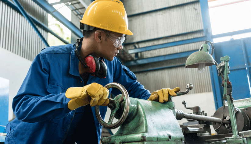 photograph of a factory worker in protective gear turning the wheel on a table-mounted machine