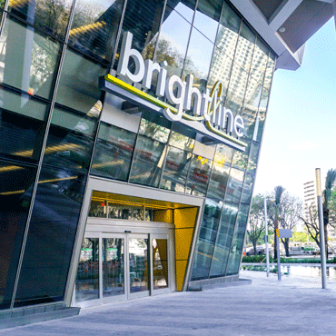 entrance to new glass front building with high rise under construction in background