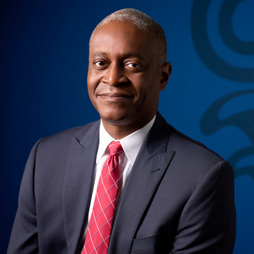 Portrait of Raphael Bostic in front of a blue screen with part of bank column logo