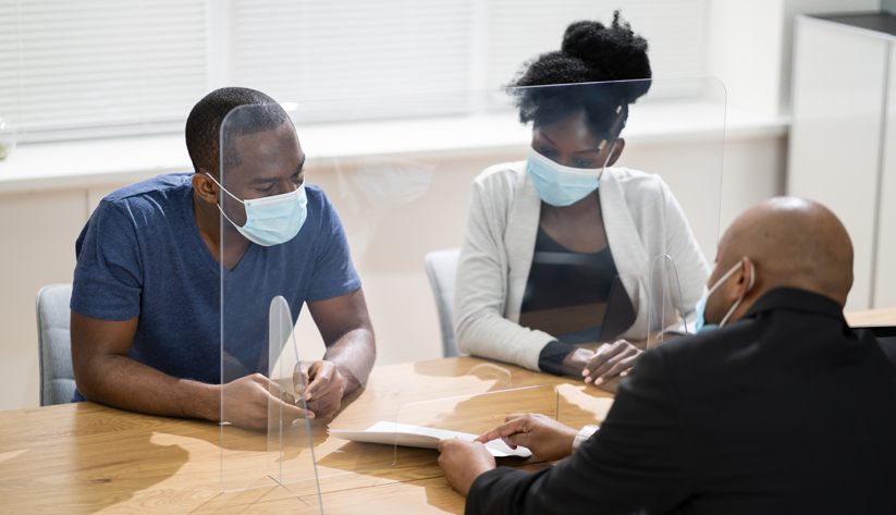 A couple talking through safety-glass barrier with professional all wearing masks