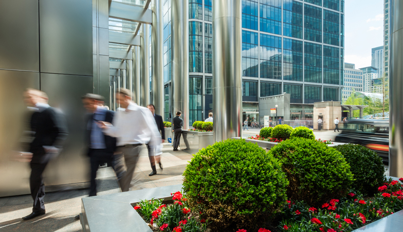 blurred people in suits walking by tall buildings and greenery