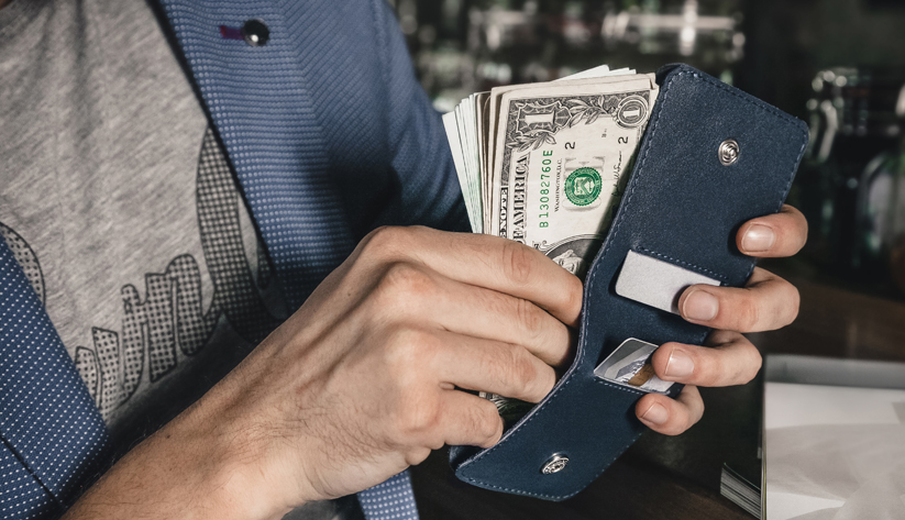 A person putting cash into a wallet.