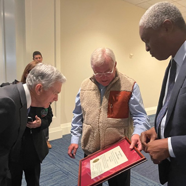 Fed chair Jerome Powell and Atlanta Fed president Raphael Powell look at Greg Waters's bank examiner commission certificate.