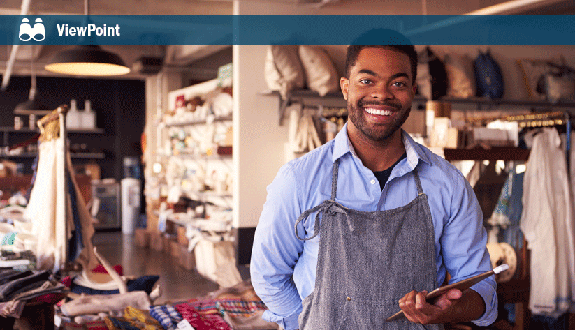 aproned man standing in foreground with upolstery materials and workspace in background