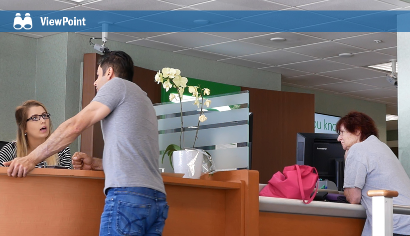 Customer gesturing while speaking with bank teller at counter as another employee works in the background
