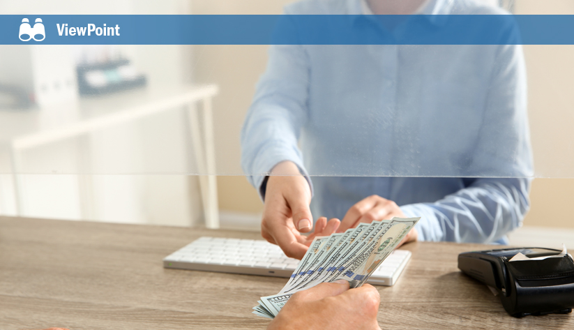 Person in blue shirt counting US dollar bills at desk with calculator and wallet nearby