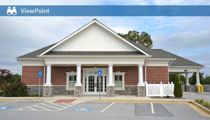 Brick building with white columns and triangular pediment, featuring accessible parking spaces and entrance ramp in front