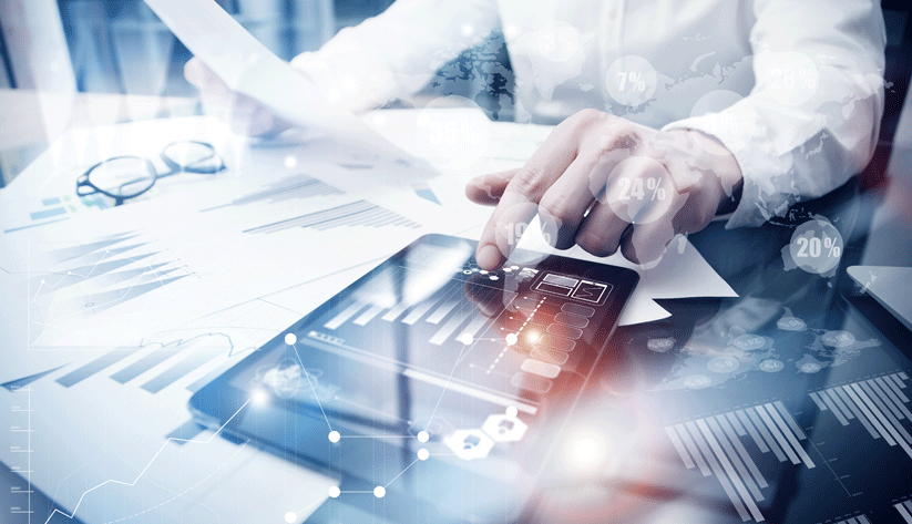person touching tablet on top of paper pile with blue tinted chart and data overlay
