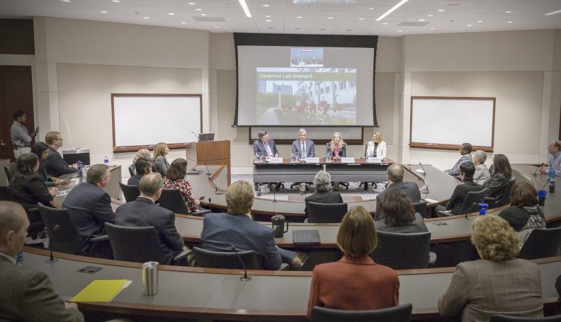 audience facing panel of four people at front of room with projector screen