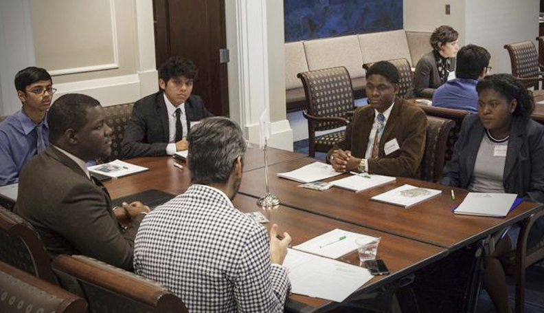 group of five seated men surrounding conference table