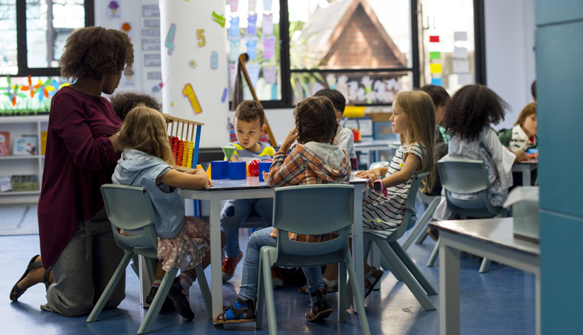 children sitting around table with teacher next to them