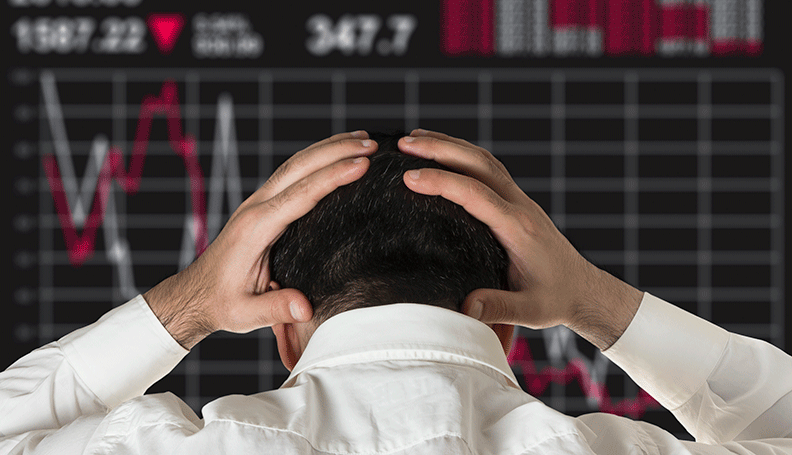 man clasping his head while looking at stock market