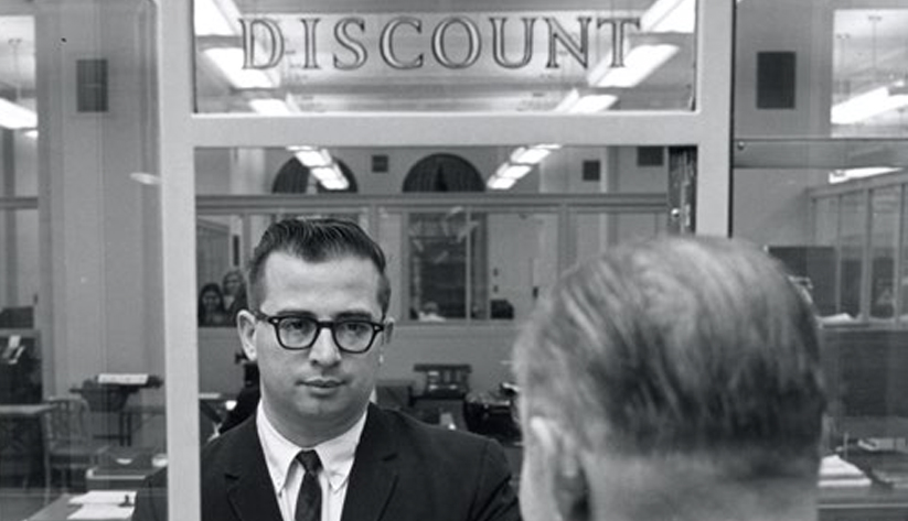 Black and white photo of a bank teller and customer at a discount window