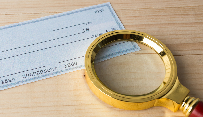 Blank blue check with gold magnifying glass laying on the bottom right corner