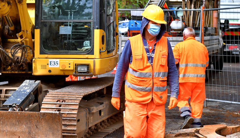 construction worker in safety gear and mask on work site with machinery