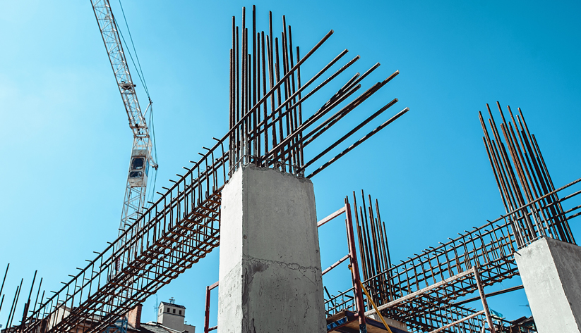 Construction site where reinforced concrete structures are being built with a large crane in the background.