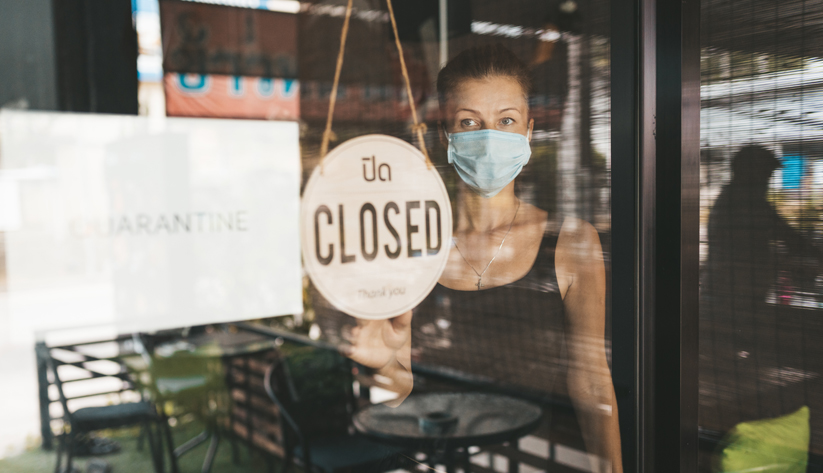 masked woman looking through glass window with closed sign