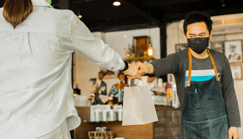 retailer handing over purchase with a mask on