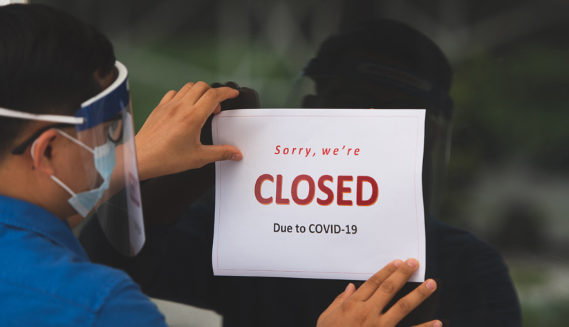 man wearing face shield hanging sorry we are closed sign