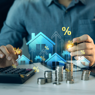 Man using a calculator with stacks of coins with houses and upward pointing arrows superimposed