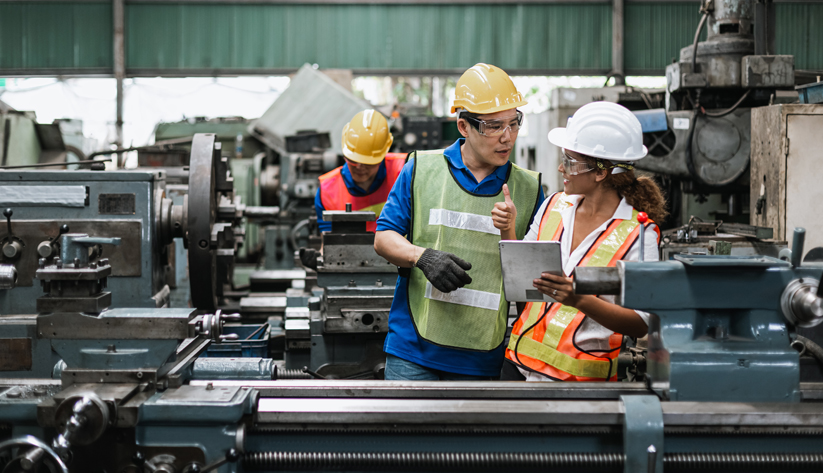 Three workers in factory wearing protective gear, working.
