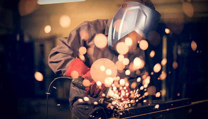 man with welding mask on welding with sparks flying at the viewer