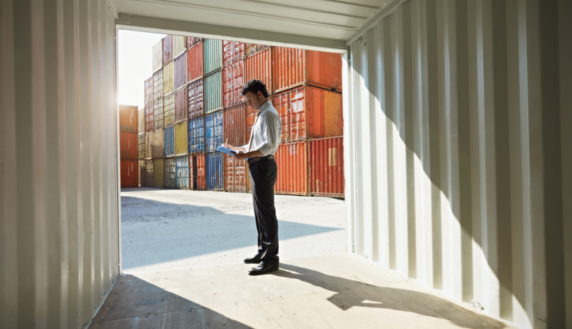 Man standing in entrance of shipping container with shipping containers in the background