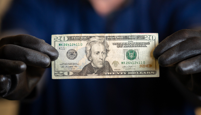 Black gloved hands holding a twenty dollar bill