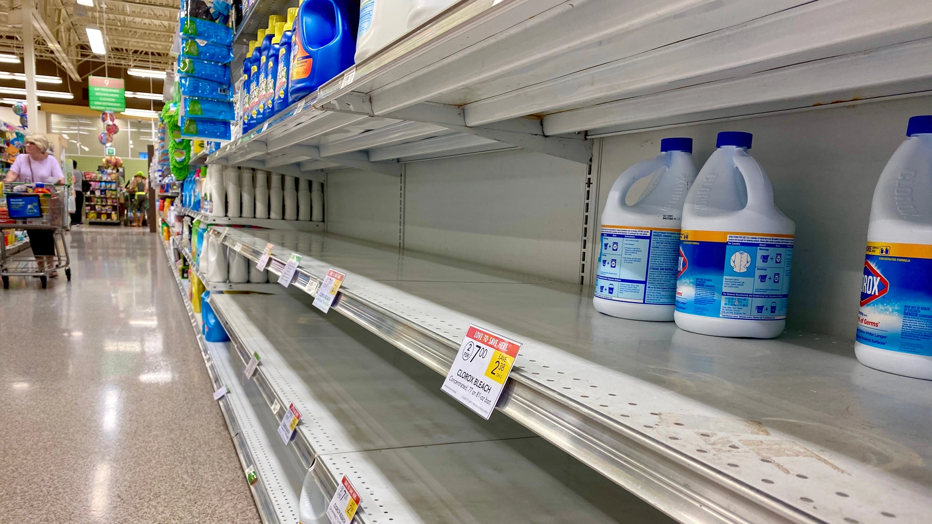 shelf with only few bottles of bleach in foreground of big box store aisle