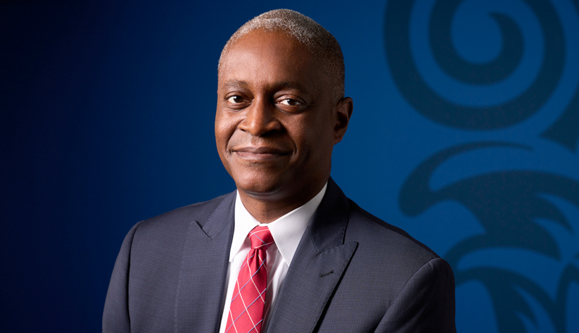 Portrait of Raphael Bostic in front of a blue screen with part of bank column logo