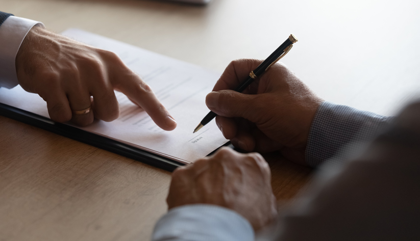 a hand pointing where to sign paper for other person holding pen