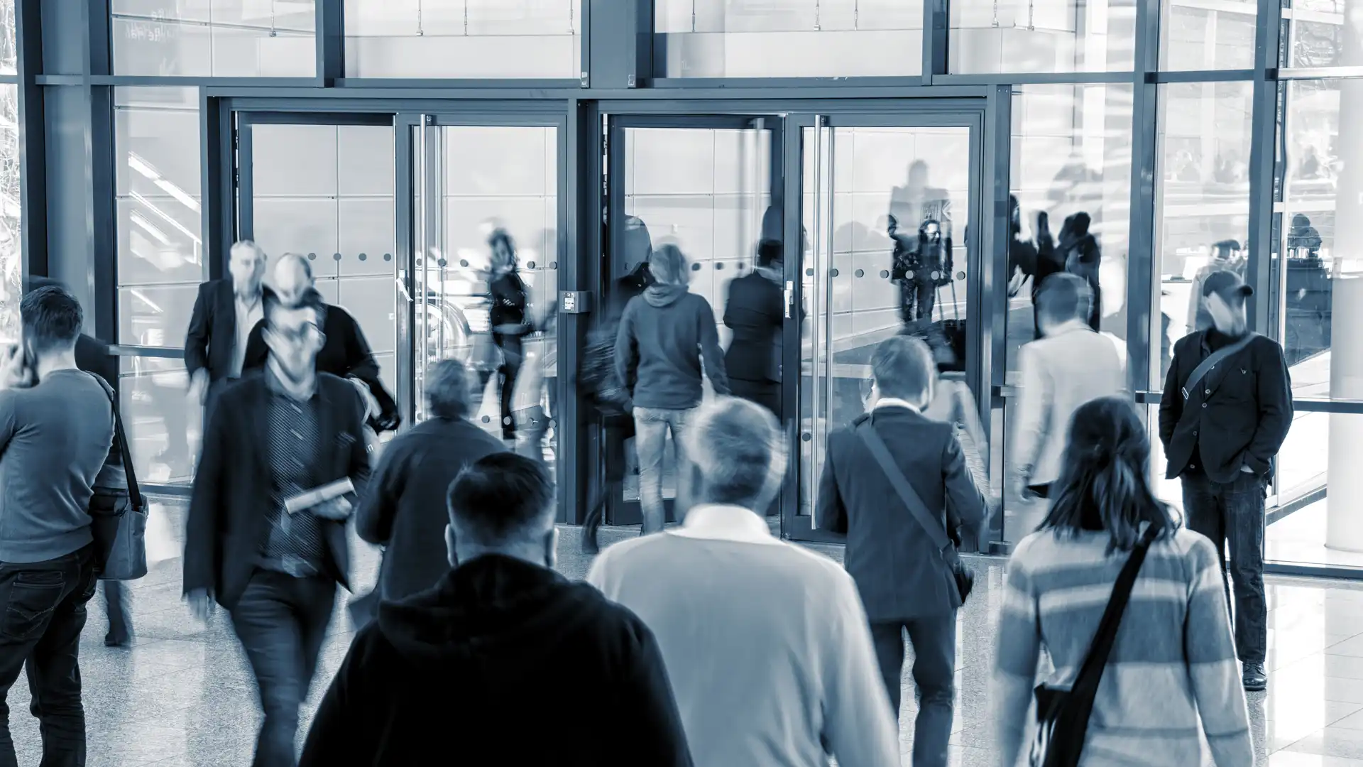 grayscale photograph of people coming from and going into building via revolving doors 