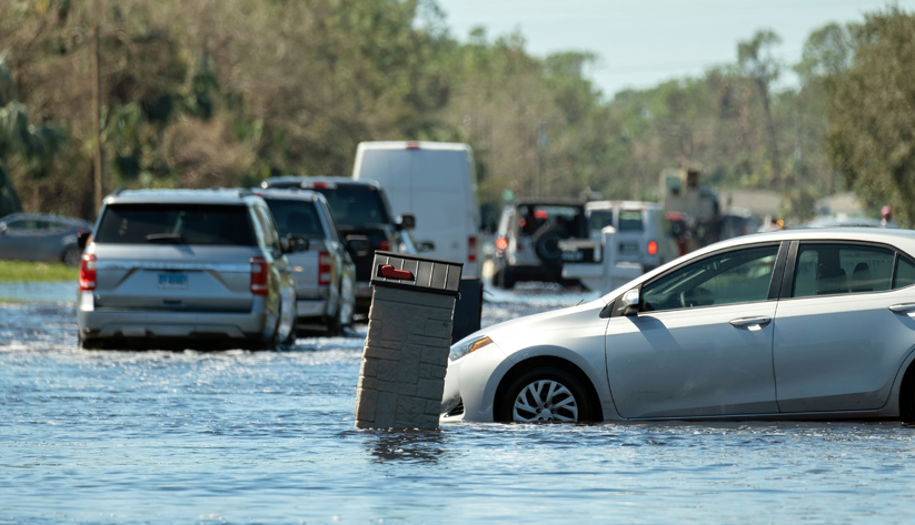 Many vehicles in a flooded street with some partially submerged object in the foreground.