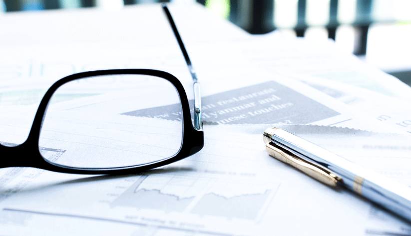 close-up photo of a pair of reading glasses, a pen, and papers on a desk