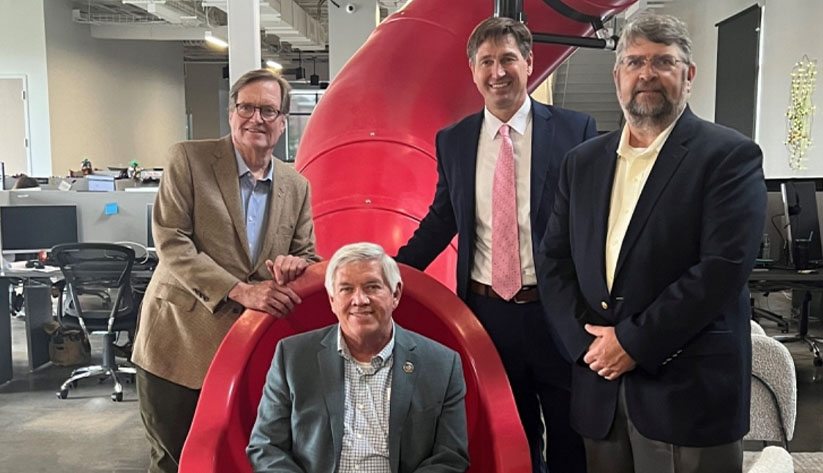 Four men in office surrounding large red slide