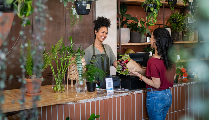 Flower store merchant handing customer bouquet of flower