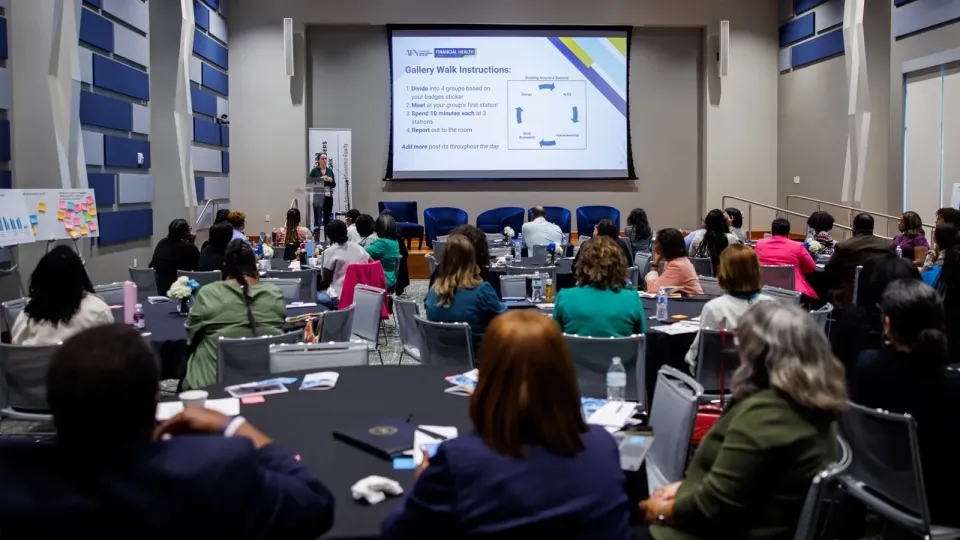A crowded room of financial coaches listen as a Fed researcher outlines the data walk.