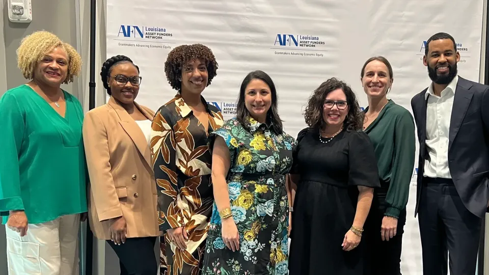 The seven event planners stand in front of a large logo banner.