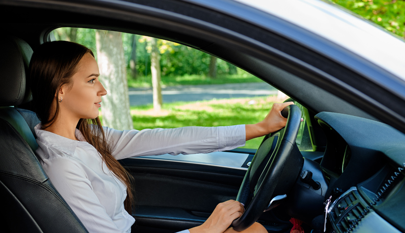 photograph of a young woman driving a car on a sunny day