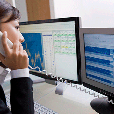 woman on telephone in front of data on computer screens